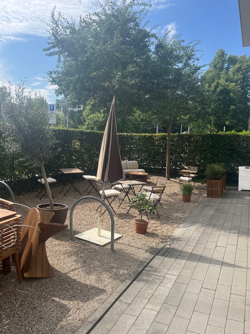 The Frame Berlin: Gartencafé mit Sonnenschirm und Blick ins Grüne