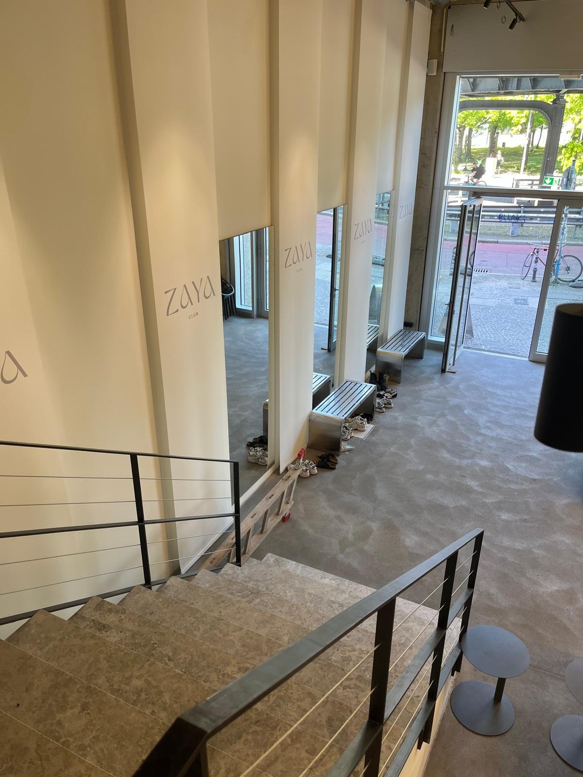 ZAYA Club Eingang: Blick von der Treppe auf den Empfangsbereich mit ZAYA Logo und Glasfront zur Straße