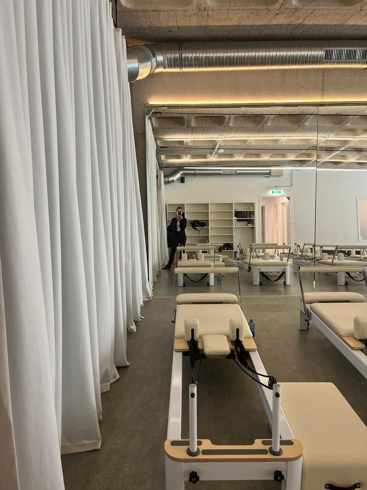 ZAYA Pilates Trainingsraum: Seitenansicht mit weißen Vorhängen, Reformern und Spiegelwand