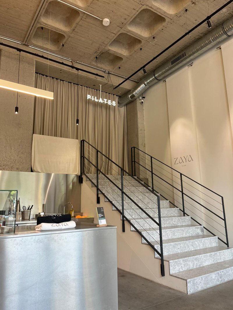 Empfangsbereich mit PILATES Neonschrift und Treppe zum Studio